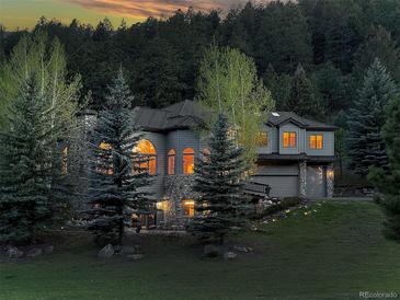 Two-story home with stone accents, arched windows and well-manicured lawn at dusk at 2191 Baldy Ln, Evergreen, CO 80439