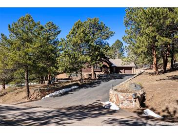 Charming home with a rustic exterior, mature trees, and a paved driveway leading to an attached garage at 2851 Interlocken Dr, Evergreen, CO 80439