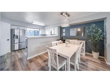 Bright dining room features stylish chandelier, white table set, accent wall and wood floors at 12069 Monaco Ct, Brighton, CO 80602
