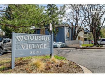 Exterior view of Woodside Village condominiums with a prominent sign showcasing the community name and street address at 8600 E Alameda Ave # 17-105, Denver, CO 80247