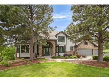 Stunning exterior view with a stone archway, stone accents, lush lawn, and mature trees on a sunny day at 920 Shady Oak Ln, Castle Pines, CO 80108