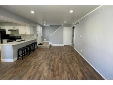 Open-concept living area with kitchen bar, wood floors, and neutral wall color provides flexible living at 2441 S Xanadu Way # A, Aurora, CO 80014