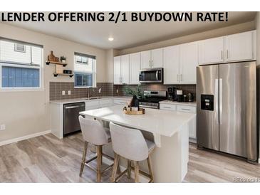 Bright kitchen features stainless appliances, white cabinets, tile backsplash, and a spacious quartz island at 1312 Independence St # 3, Lakewood, CO 80215