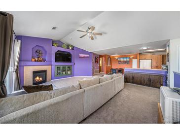 Bright, open living room featuring a fireplace, ceiling fan and adjacent kitchen space at 10818 Cimarron St # 206, Firestone, CO 80504