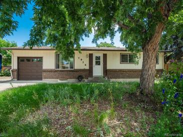 Charming single-story home featuring a brick facade, attached garage, and mature landscaping with a large shady tree at 7936 Eaton St, Arvada, CO 80003