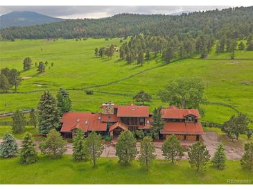 Stunning aerial view of a sprawling property with lush green fields and a charming home with a red roof at 5939 Lone Peak Dr, Evergreen, CO 80439