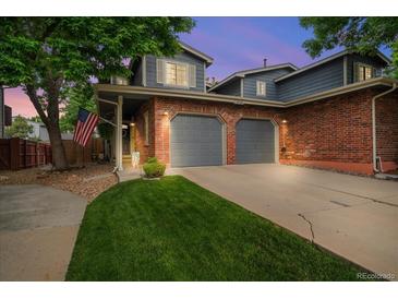 Charming two-story home features a brick facade, two-car garage, and well-manicured lawn, complemented by mature trees and an American flag at 12545 Elm St, Thornton, CO 80241
