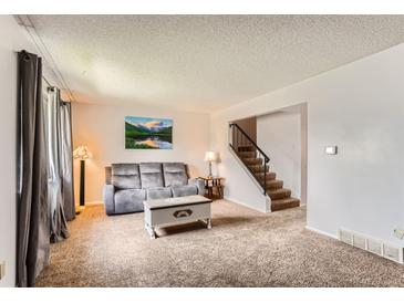 Bright living room featuring neutral carpet, gray couch, and stairs to the upper level at 8613 Santa Fe Dr, Thornton, CO 80260