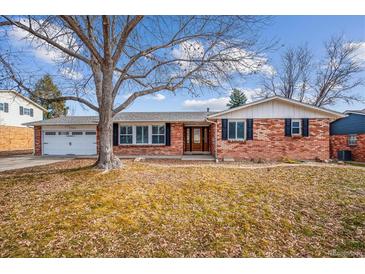Charming brick home featuring an attached two-car garage and a beautifully landscaped front yard beneath a sunny, blue sky at 7310 S Sheridan Ct, Littleton, CO 80128