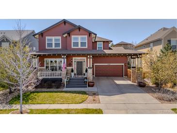 Charming two-story red home with a landscaped yard, covered porch, and attached two car garage at 13360 W 83Rd Pl, Arvada, CO 80005