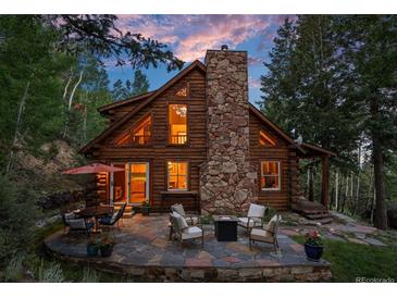 Charming log cabin with stone chimney and outdoor stone patio seating area at 80 Spruce Ct, Evergreen, CO 80439