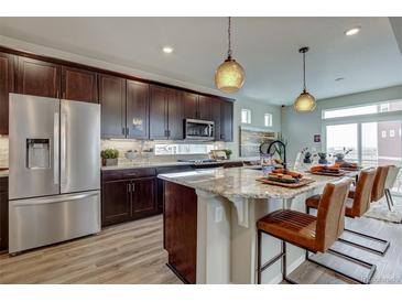 Gourmet kitchen featuring dark wood cabinetry, stainless steel appliances, and a large granite island with bar seating at 1158 Sugarloaf Ln, Erie, CO 80516