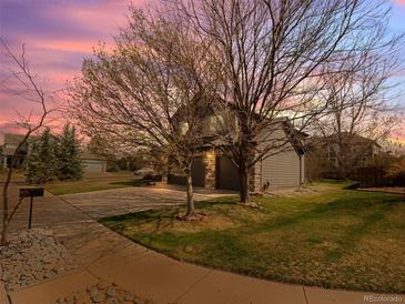 Charming home features a two-car garage, green lawn, and mature trees against a picturesque sunset sky at 11910 W 83Rd Pl, Arvada, CO 80005