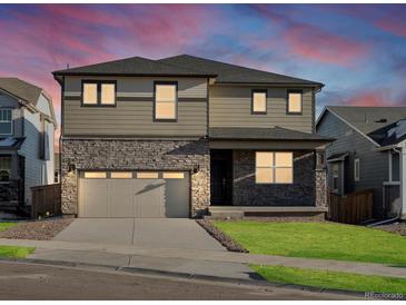 Two-story home with a stone facade, gray siding, and well-maintained lawn at sunset at 6156 Hourglass Dr, Brighton, CO 80601