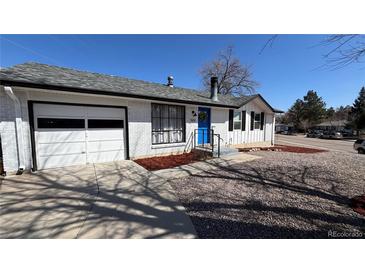 Charming single-story home with a blue front door, white brick, attached garage, and landscaped yard at 7604 Reed St, Arvada, CO 80003