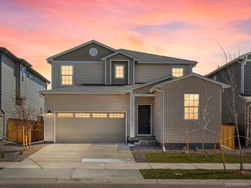 Charming two-story home with a brick facade, attached garage, and manicured lawn under a vibrant sunset sky at 552 Red Rock Pl, Brighton, CO 80601