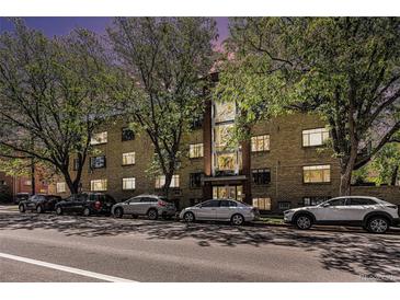 An exterior view of a multi-unit residential building on a tree-lined street with many parked cars at 500 E 11Th Ave # 102, Denver, CO 80203
