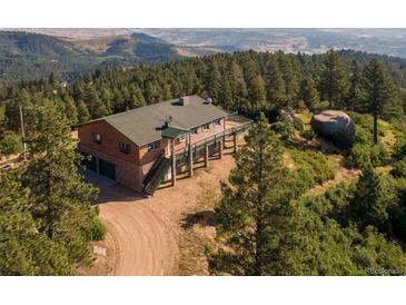 Stunning log home featuring an outdoor deck and a two-car garage nestled amid lush green trees and mountain scenery at 2518 N State Highway 67, Sedalia, CO 80135