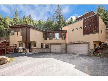 A contemporary two-story home nestled in a wooded setting, featuring a large driveway and attached two-car garage at 30174 Glen Eyrie Dr, Evergreen, CO 80439