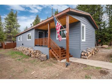 Charming single-story home with a covered porch, wood piles, and an American flag at 192 Little Creek Rd, Idaho Springs, CO 80452