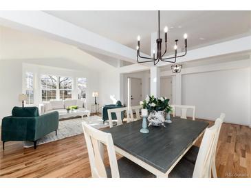 Bright, open-concept dining area featuring modern chandelier, hardwood floors, and view into the living room at 8896 Goosander Way, Littleton, CO 80126