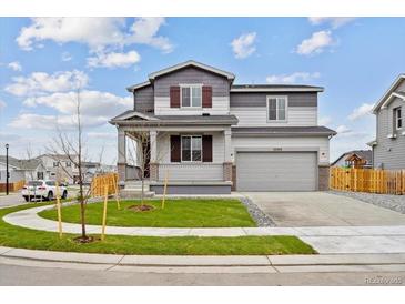 Charming two-story home featuring gray and white siding, a covered front porch, and manicured landscaping at 12353 E 101St Pl, Commerce City, CO 80022