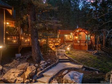 Charming log cabin home with stone walkway, wooden decks, and beautiful outdoor lighting at 30264 Upper Bear Creek Rd, Evergreen, CO 80439