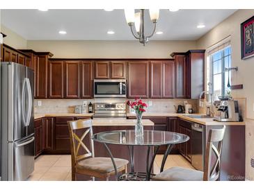 Bright kitchen featuring stainless steel appliances, dark wood cabinets, and a glass dining table at 17035 E 102Nd Pl, Commerce City, CO 80022