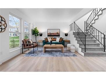 Bright living room features a teal sofa, wood floors, and modern staircase at 12054 E 3Rd Ave, Aurora, CO 80011