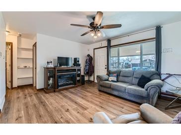 Inviting living room features wood floors, a ceiling fan, fireplace, and a large window for natural light at 7940 Pontiac St, Commerce City, CO 80022