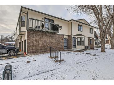 Charming townhome showcasing a brick facade, second-story deck and snowy front yard at 1760 S Ammons St # D, Lakewood, CO 80232