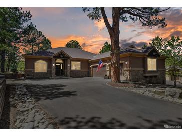 Charming single-story home featuring a stone facade, well-lit driveway, and an American flag, set against a vibrant sunset sky at 670 Independence Dr, Larkspur, CO 80118