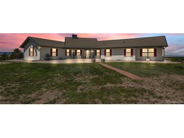 Charming single-story home with a metal roof, large windows, red shutters and well-kept lawn at sunset at 30999 Kootney St, Elizabeth, CO 80107