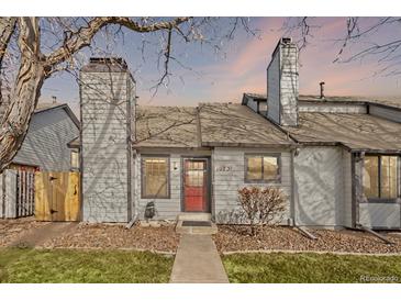 Charming townhome featuring light gray siding, red front door, chimney and lovely landscaping at 10731 W 63Rd Ave # A, Arvada, CO 80004