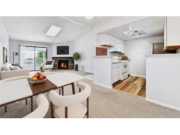Cozy living room featuring a stone fireplace, natural light, and an adjacent modern kitchen with white cabinets at 910 S Walden St # 201, Aurora, CO 80017
