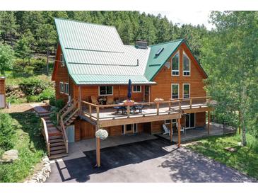 Charming home featuring a large deck with outdoor seating and lush landscaping, surrounded by beautiful trees at 10381 Hondah Dr, Littleton, CO 80127