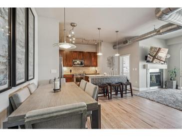 Open-concept living area with modern lighting fixtures, wood floors, fireplace and adjacent kitchen with bar seating at 10111 Inverness Main St # 230, Englewood, CO 80112