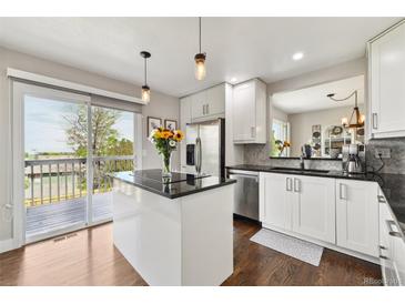 Bright white kitchen with black countertops, stainless appliances, and a door leading to an outdoor deck at 19131 E Garden Pl, Centennial, CO 80015