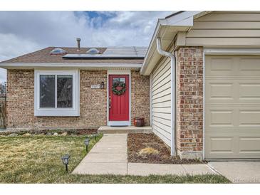 Charming single-story home featuring a brick facade, attached two-car garage, a red door, and solar panels at 5587 S Simms Way, Littleton, CO 80127