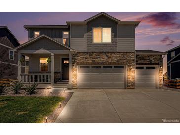 Charming two-story home features a stone facade, three-car garage, and a welcoming front porch at twilight at 7415 E 158Th Pl, Thornton, CO 80602