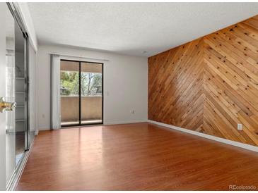 Bright living room boasts sleek hardwood floors, a private balcony, and an accent wall with herringbone wooden panelling at 3662 S Granby Way # J05, Aurora, CO 80014