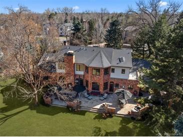 Expansive brick home featuring a spacious patio, lush lawn, mature trees, and outdoor seating area at 29 Viking Dr, Cherry Hills Village, CO 80113