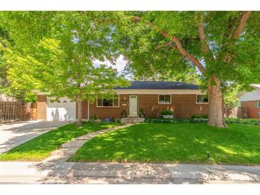 Charming brick home featuring mature trees, lush green lawn, and inviting curb appeal at 1410 S Ammons St, Lakewood, CO 80232