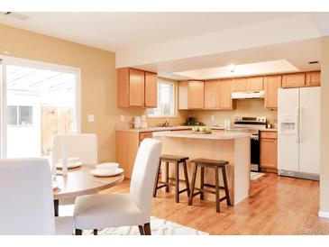 Bright kitchen features an island with bar seating, stainless steel appliances, and wood floors at 654 S Xenon Ct, Lakewood, CO 80228