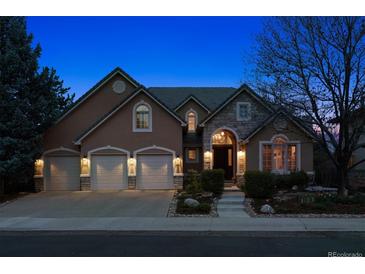 Charming home featuring a three-car garage, stone accents, and a manicured front yard, lit at dusk at 7420 S Wolff St, Littleton, CO 80128