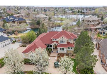 Stunning aerial view of a luxury home with a red roof, beautiful landscaping, and a serene lake in the background at 16 Blue Heron Dr, Thornton, CO 80241