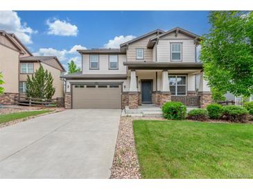 Charming two-story home featuring a manicured lawn and a welcoming front porch with stone accents at 676 Fossil Bed Cir, Erie, CO 80516