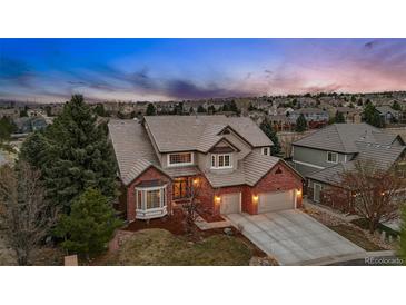 Striking two-story home with red brick, neutral siding, mature trees, and a well-manicured lawn at dusk at 7086 Esperanza Dr, Castle Pines, CO 80108