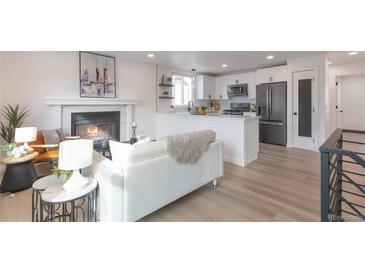 Bright living room featuring a modern fireplace, open to the kitchen with stainless steel appliances and white cabinetry at 9306 Clermont Dr, Thornton, CO 80229