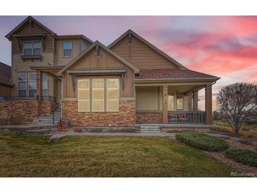 Charming townhome with stone accents, covered porch, and manicured lawn at dusk at 555 Gallegos Cir, Erie, CO 80516